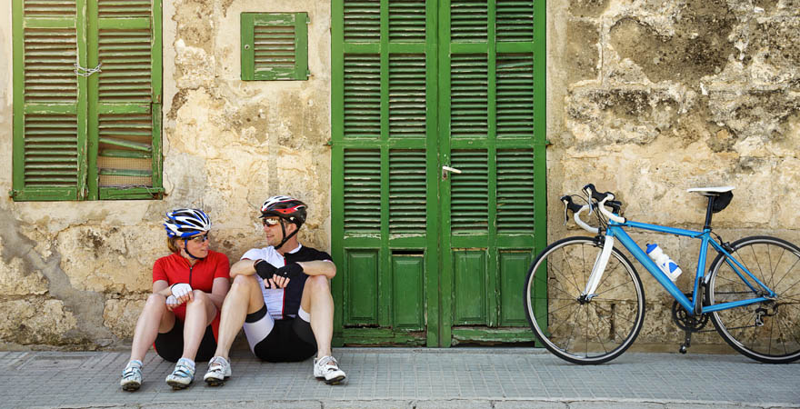 Radfahrer und Radfahrerin sitzen am Boden, daneben ein blaues Fahrrad