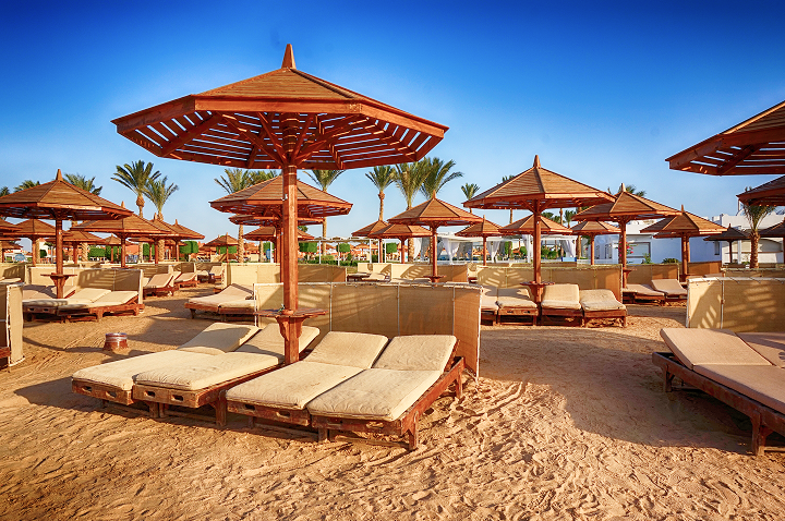 Strahlender Sonnenschein beleuchtet eine Reihe von modernen Sonnenschirmen am Strand. Strahlender Sonnenschein beleuchtet eine Reihe von modernen Sonnenschirmen am Strand.