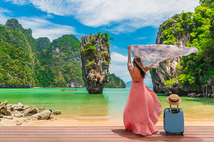 Auf einem Dock in Thailand steht eine Frau in einem pinken Kleid mit einem Koffer. Auf einem Dock in Thailand steht eine Frau in einem pinken Kleid mit einem Koffer.