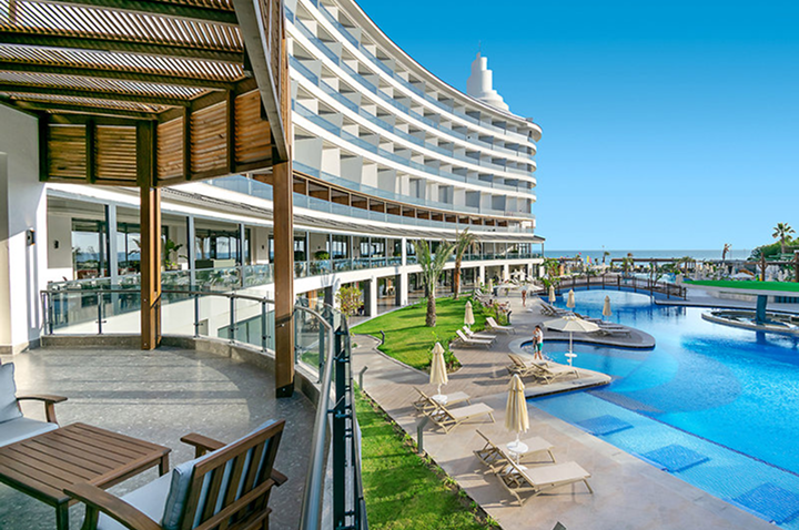 Blick auf einen geschwungenen Hotelkomplex mit Pool, Liegestühlen und Sonnenschirmen auf der Terrasse Blick auf einen geschwungenen Hotelkomplex mit Pool, Liegestühlen und Sonnenschirmen auf der Terrasse