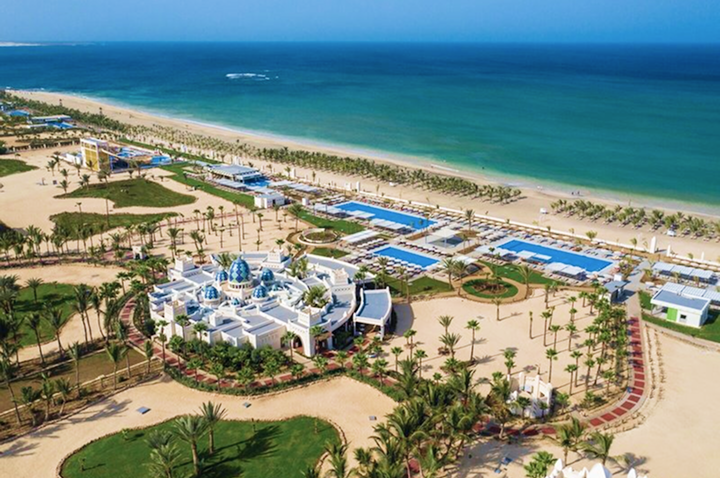 Luftaufnahme eines Resorts mit weiß-blauen Gebäuden, mehreren Pools, Palmen und einem Sandstrand am Meer Luftaufnahme eines Resorts mit weiß-blauen Gebäuden, mehreren Pools, Palmen und einem Sandstrand am Meer