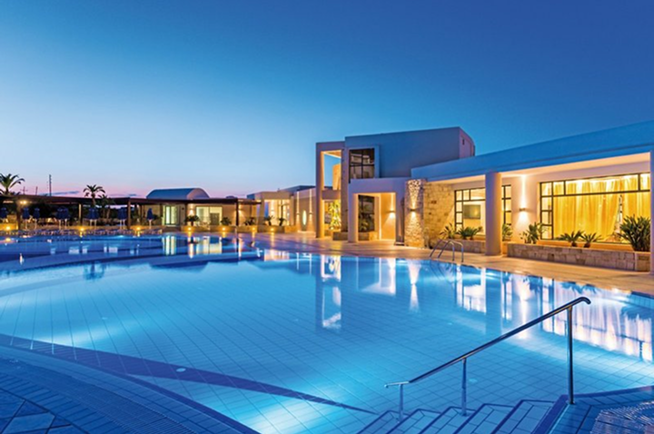 Großer beleuchteter Hotelpool mit moderner Architektur im Hintergrund bei Dämmerung. Großer beleuchteter Hotelpool mit moderner Architektur im Hintergrund bei Dämmerung.