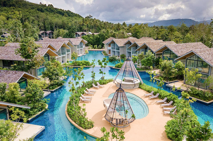 Resort mit mehreren zweistöckigen Bungalows um einen großen Pool mit Sandinsel und Hängesesseln, umgeben von grünen Hügeln. Resort mit mehreren zweistöckigen Bungalows um einen großen Pool mit Sandinsel und Hängesesseln, umgeben von grünen Hügeln.