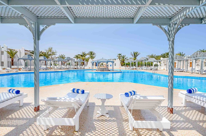 Großer Pool mit Liegen und Sonnenschirmen unter einem weißen Pavillon in einer Hotelanlage mit Palmen im Hintergrund. Großer Pool mit Liegen und Sonnenschirmen unter einem weißen Pavillon in einer Hotelanlage mit Palmen im Hintergrund.