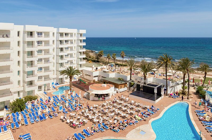 Hotelanlage mit mehreren Stockwerken, Pool, vielen Liegestühlen und Tischen auf der Terrasse sowie Strand und Meer im Hintergrund Hotelanlage mit mehreren Stockwerken, Pool, vielen Liegestühlen und Tischen auf der Terrasse sowie Strand und Meer im Hintergrund